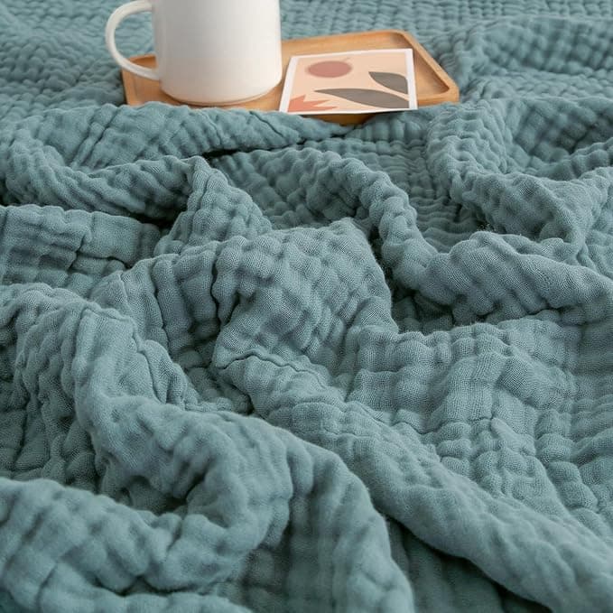 Oversized chunky hand-knit chenille throw blanket in oatmeal draped over a sofa arm